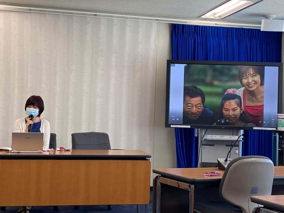 Woman speaking with microphone and tv with pictures is on in the background